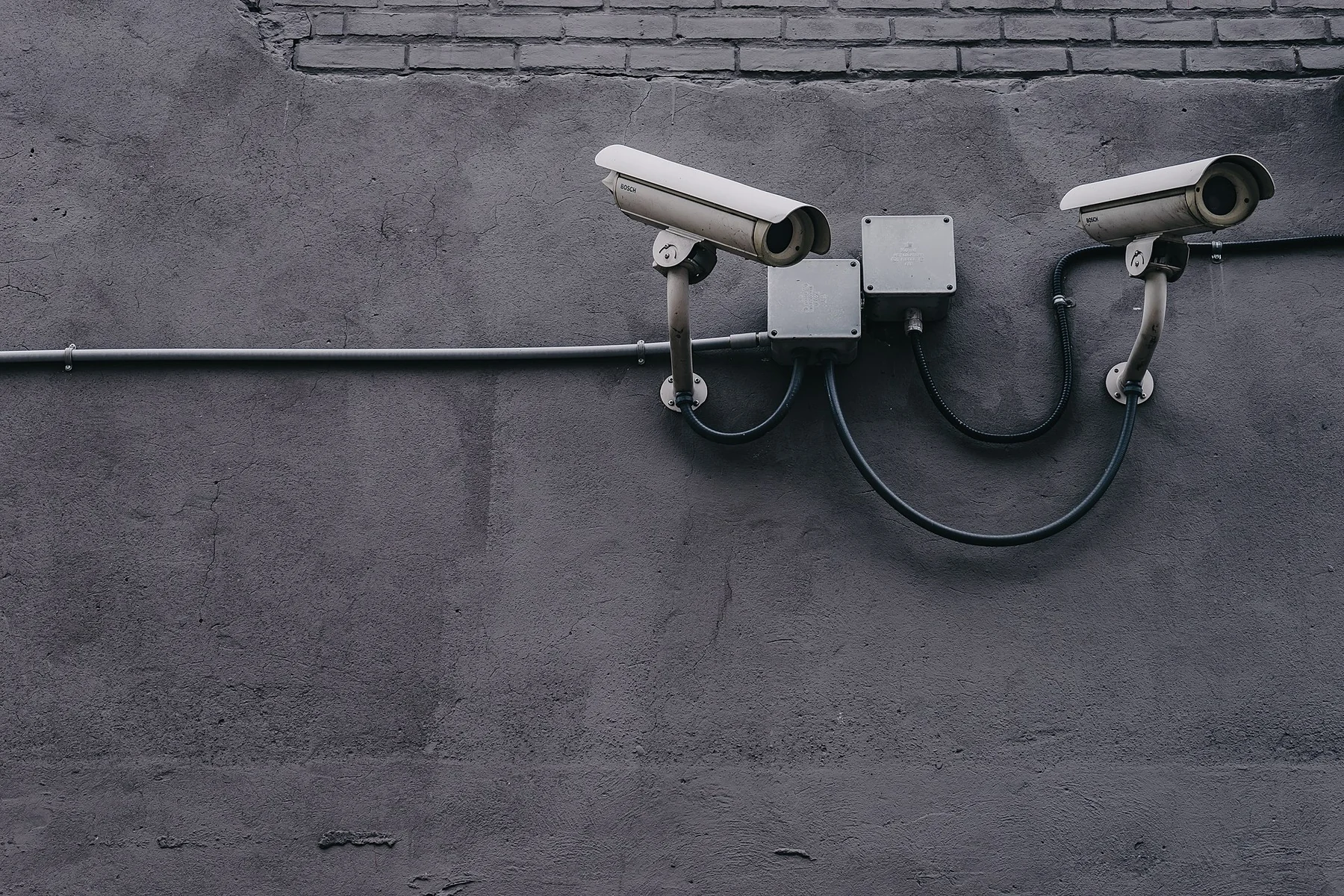 Two real outdoor surveillance cameras mounted on a concrete wall